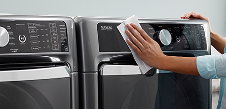 A person wipes down a washing machine control panel.