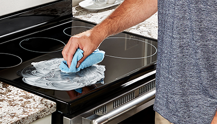 A person applies cooktop cleaner to a glass cooktop.