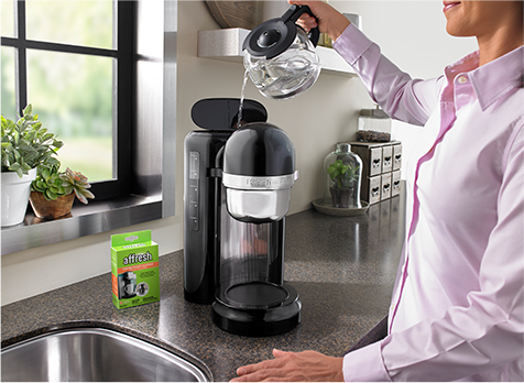 A person pours water into a coffee maker reservoir.