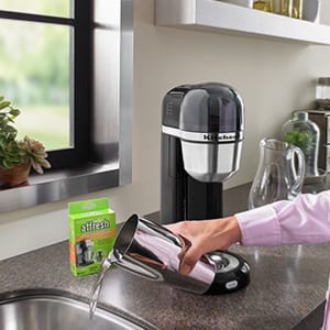A woman pours the solution down the drain after using affresh Coffee Maker Cleaner tablets to clean and descale her KitchenAid coffee machine.