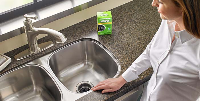 A woman admires the clean garbage disposal after cleaning with affresh disposal cleaner.