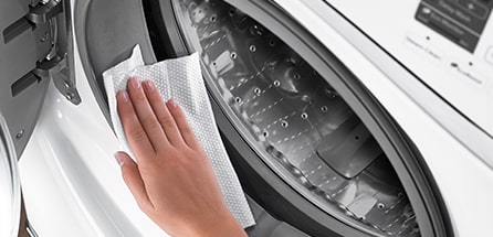 A person wiping down the rubber gasket of a front loading washing machine.