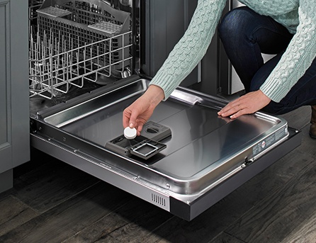 A person places a dishwasher cleaning tablet in the detergent dispenser.