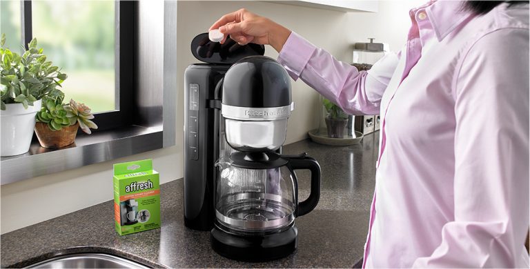 A person places an affresh coffee maker cleaner tablet in a coffee maker’s water reservoir.