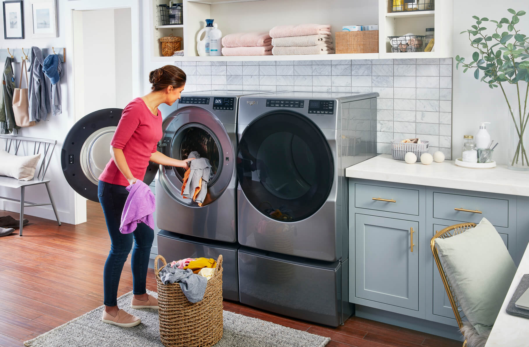 A woman loads clothes into a front-load washing machine in her laundry room.