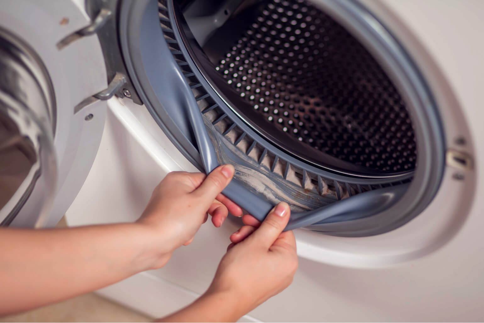 A person pulling back the rubber door gasket on a front load washer to expose dirt build-up.