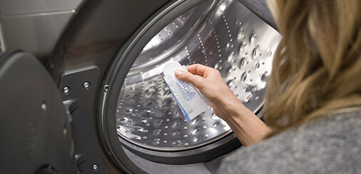 A person wiping down the rubber gasket of a front loading washing machine.