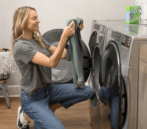 A woman wipes down and cleans the inside of a washing machine.