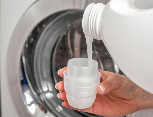 A person pouring liquid bleach into the detergent cup to sanitize a washing machine.