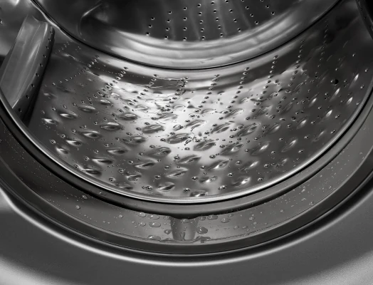 Close-up view inside a top-load washing machine drum, showing a textured stainless steel surface covered in water droplets and small puddles.