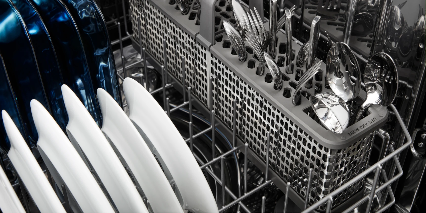 Close-up of a dishwasher rack with white plates, a blue pan, and a silverware basket of utensils