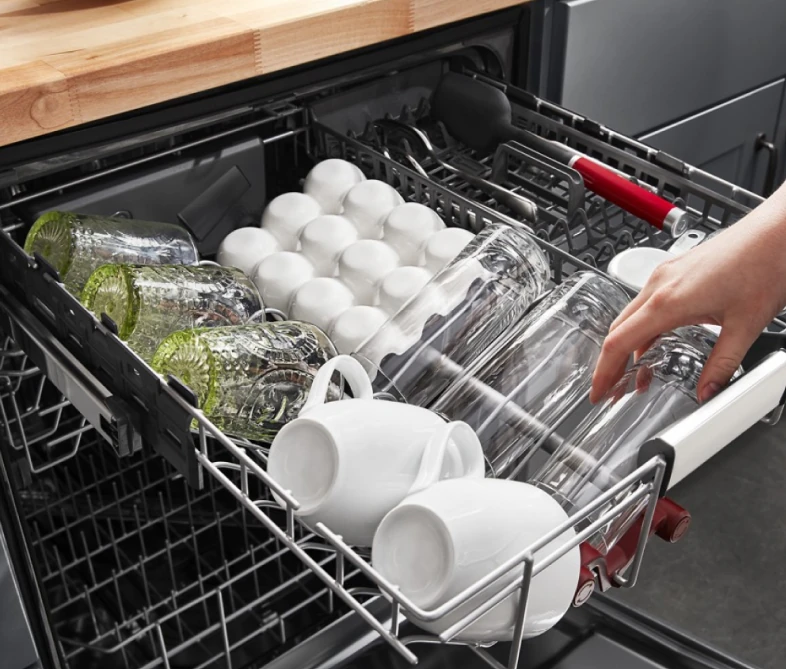 Hand loading glasses and white mugs onto a dishwasher third rack