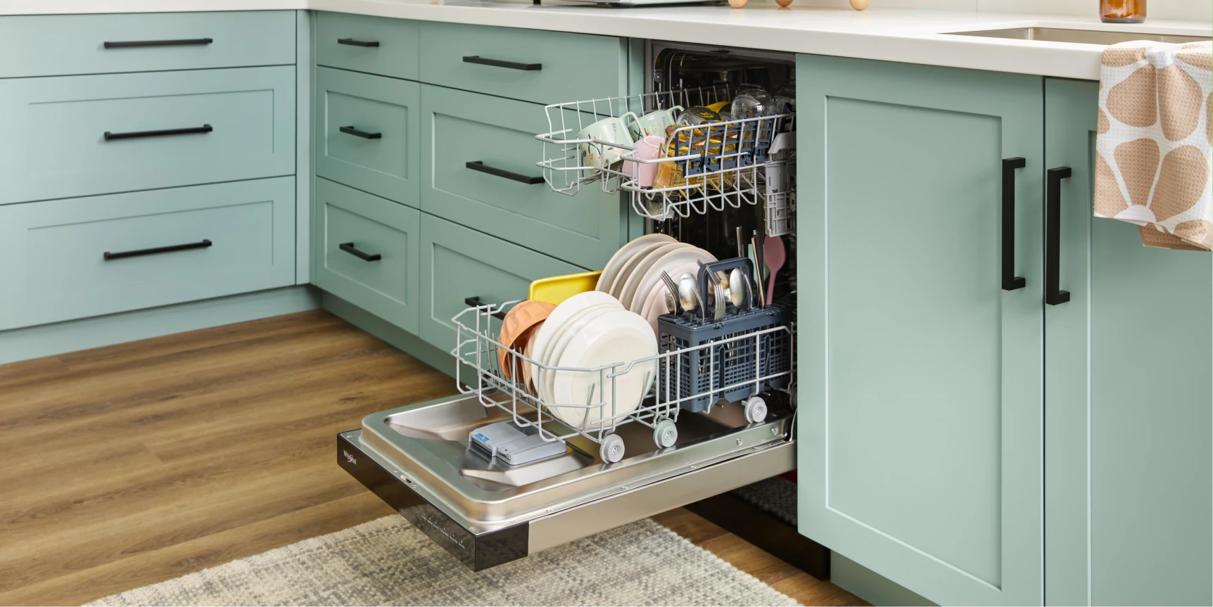 Open dishwasher loaded with plates, bowls, cups, and silverware in a mint-green kitchen