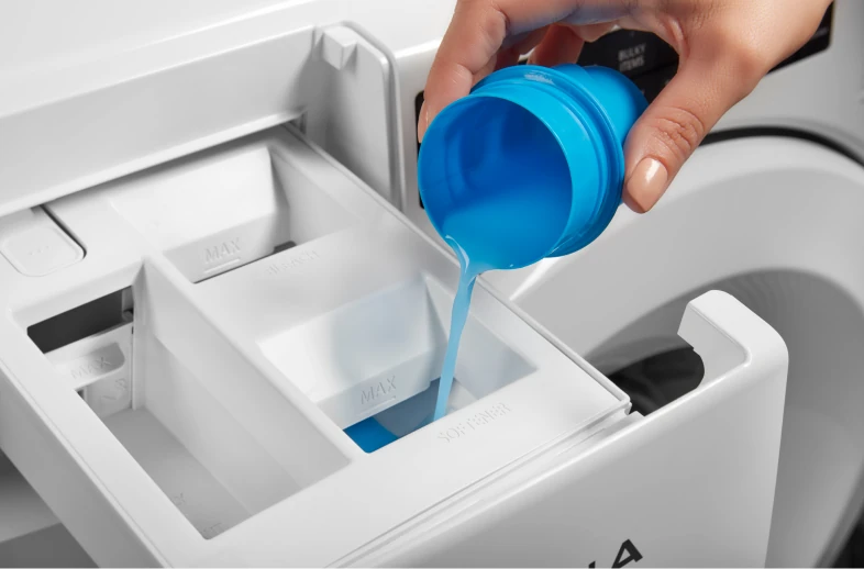 Hand pouring blue liquid fabric softener into a washing machine dispenser drawer