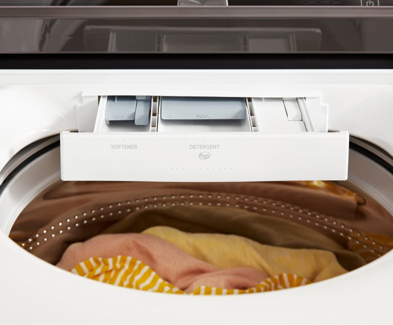 Front-load washer dispenser drawer labeled Softener and Detergent above a load of laundry