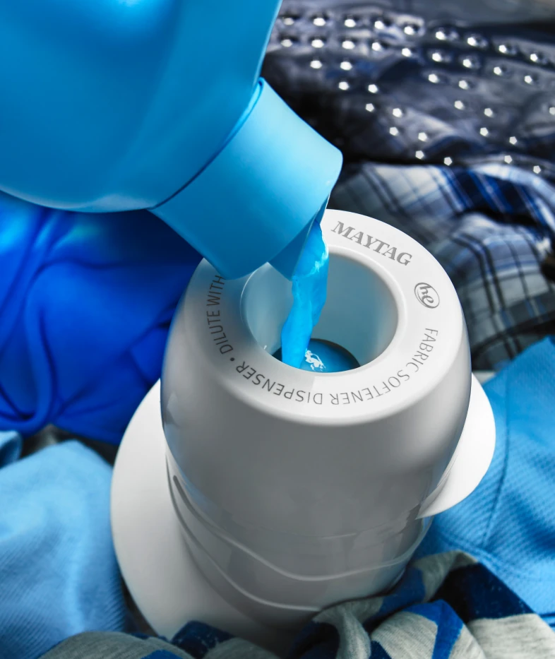 Pouring blue fabric softener into a Maytag top-load fabric softener dispenser