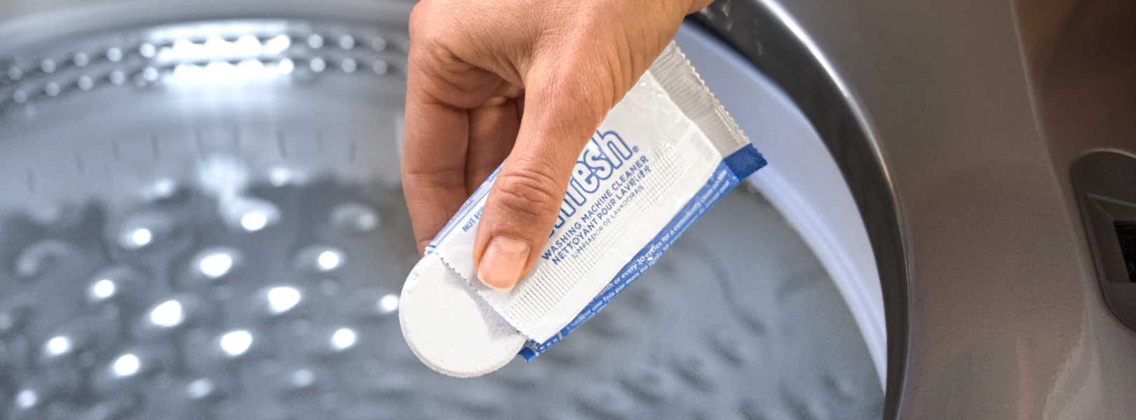 Hand adding an affresh washing machine cleaner tablet to a front-load washer drum